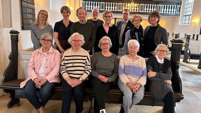 En gruppe kvinder samlet i kirke, nogle sidder på bænke, andre står bagved