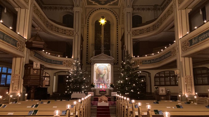In der Kirche stehen zwei Weihnachtsbäume, die mit Lichtern geschmückt sind.