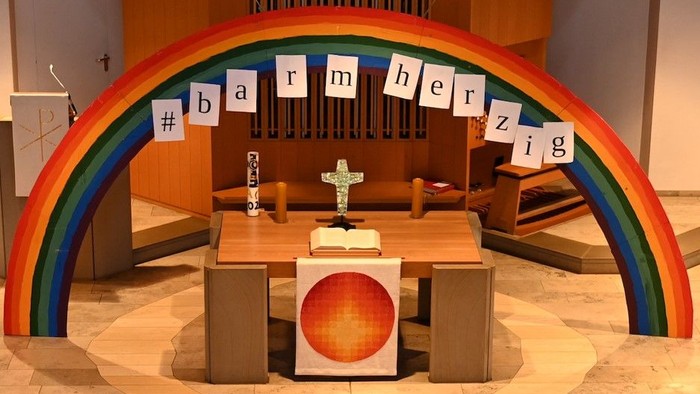 Bunte Regenbogeninstallation in Kirche mit Kreuz und Texten