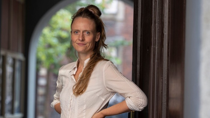 En kvinde står i en døråbning og smiler.