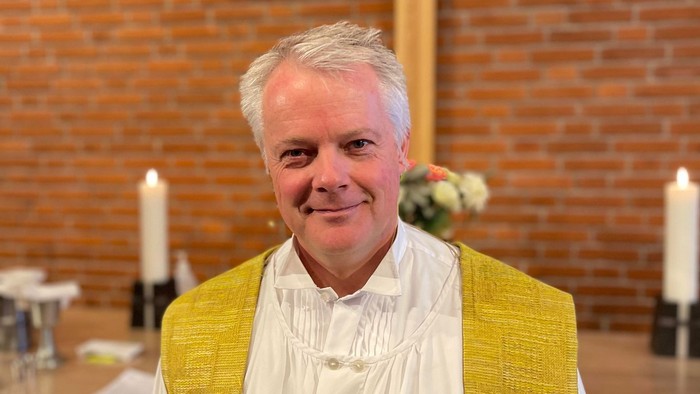 Mand i kirkeklæder foran kors og lysestage