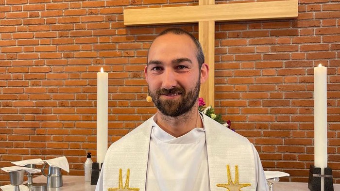 Mand i religiøs kappe foran kors og lysestake