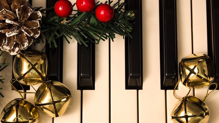 Weihnachtliche Klavierdekoration mit goldenen Glöckchen und Tannenzapfen