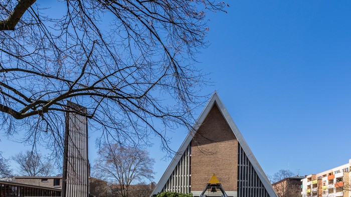 Ein modernes Gebäude mit dreieckigem Dach neben einem Baum und einem Parkplatz.