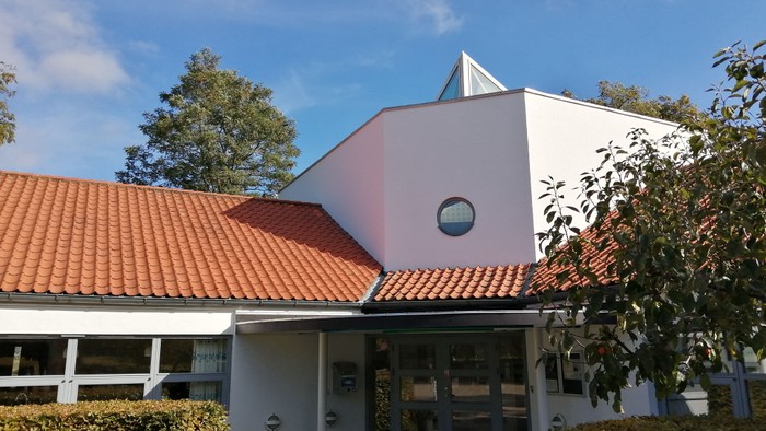 Hus med rødt tag og rund vindue, med en fugl i luften