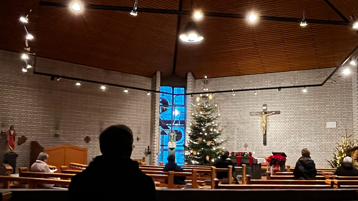 In der Kirche sitzen Menschen vor Weihnachtsbaum und Krippe.