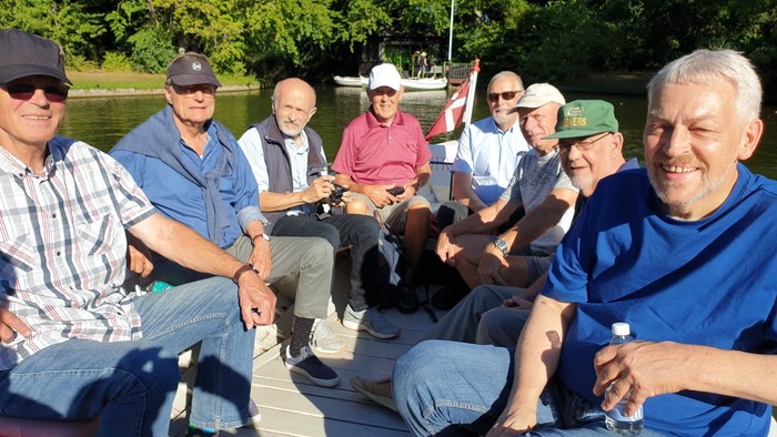 En gruppe mænd sidder på en bro over et vandløb og smiler til kameraet