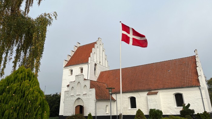 En hvid kirke med røde tag og en dansk flag på en stang foran