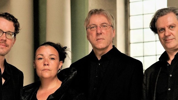 Vier Personen posieren gemeinsam – drei Männer und eine Frau –, alle in formeller Kleidung.