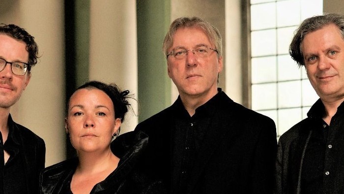 Vier Personen posieren gemeinsam – drei Männer und eine Frau –, alle in formeller Kleidung.