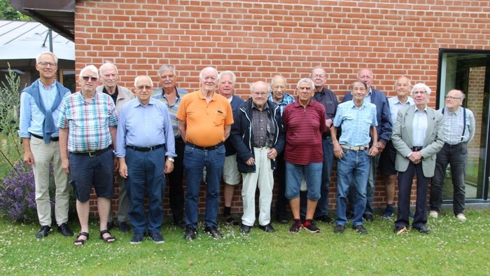 En gruppe af ældre mænd står sammen udenfor et rødt murstenshus.