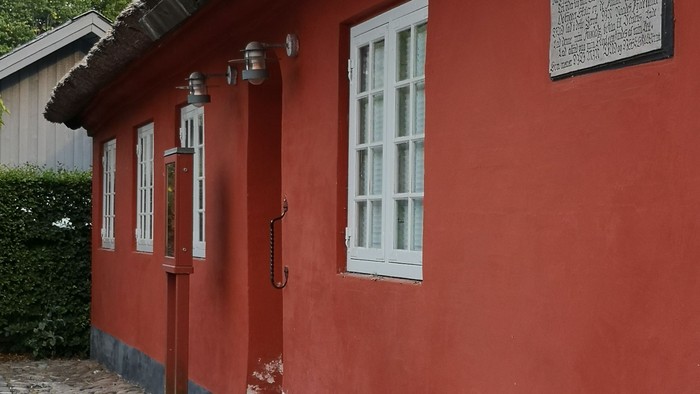 Rødt hus med hvide vinduer og skilt på væggen