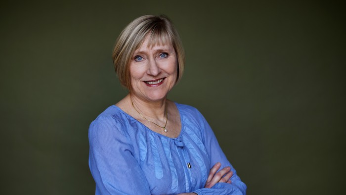 En kvinde i blå bluse med armene krummet og en smilende udtryk.