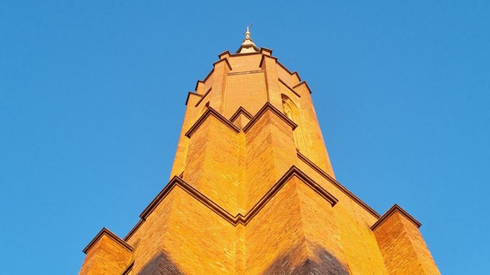 Das Bild zeigt einen hohen, spitzen Turm vor einem klaren blauen Himmel.