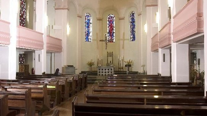 Innenraum einer Kirche mit Holzbänken und bunten Kirchenfenstern