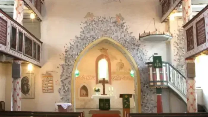 Kircheninneres mit aufwendigen Verzierungen, Empore und Buntglasfenstern.