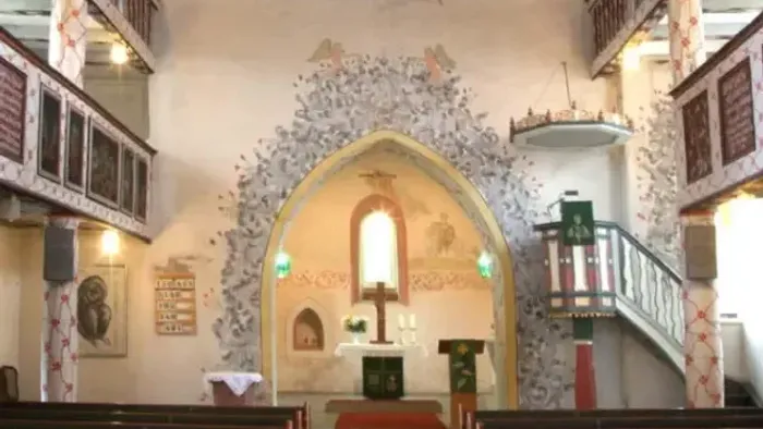 Kircheninneres mit aufwendigen Verzierungen, Empore und Buntglasfenstern.