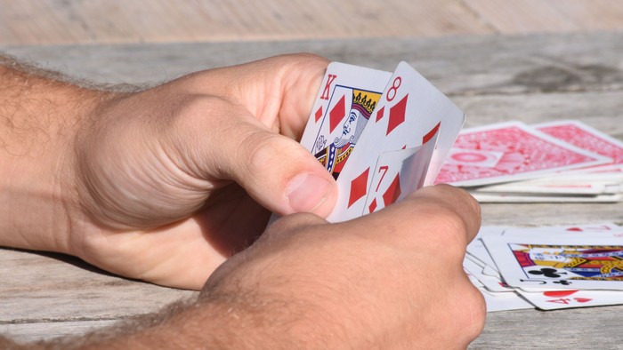 Eine Person hält Karten in der Hand, darunter die Pik-Dame und Pik-Bube.