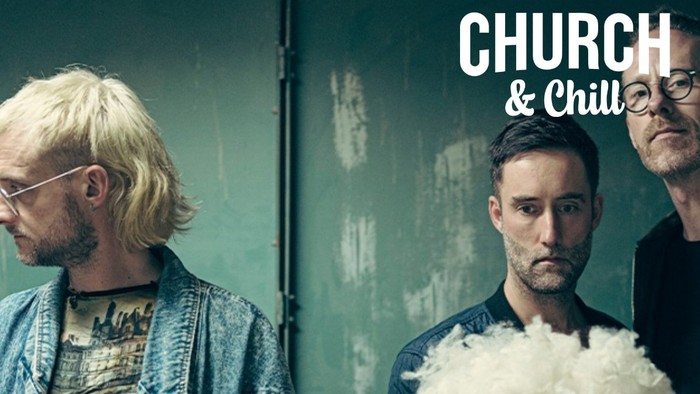 En gruppe mænd står sammen mod en grøn væg, en af dem holder en fluffy objekt