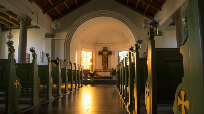 Interiør af kirke med grønne bænkehaler og lysende vinduer