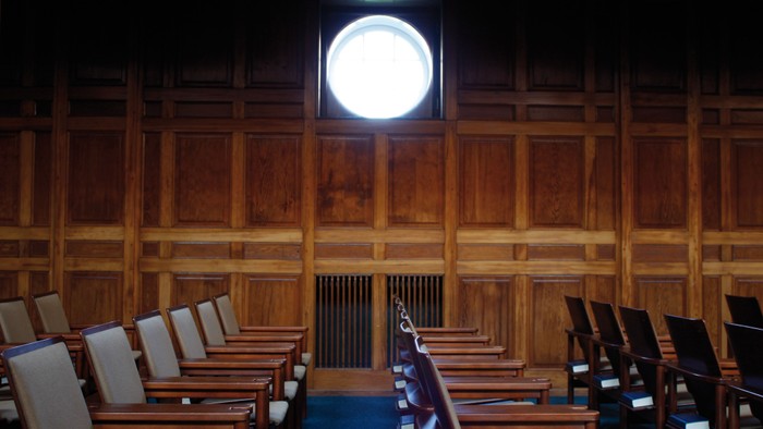 En stor, mørk sal med trævægge og rækker af stoler.