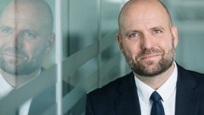 Mand i formel klædning står foran glasvæg med sit eget refleksbillede.