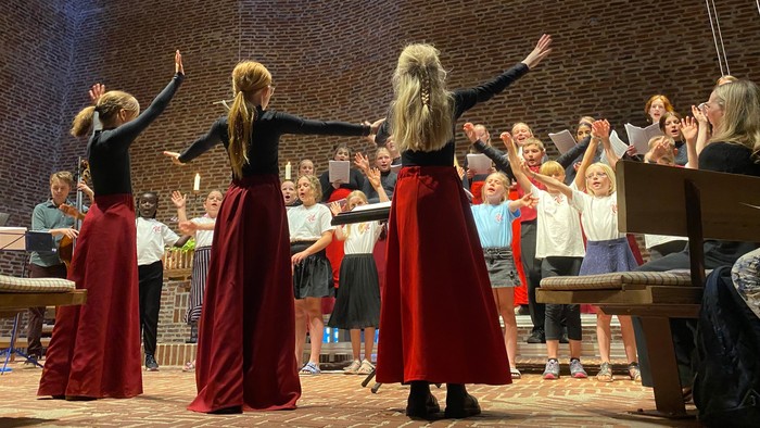 En gruppe kvinder i røde skørter og sorte topper danser på en scene foran en publikum.