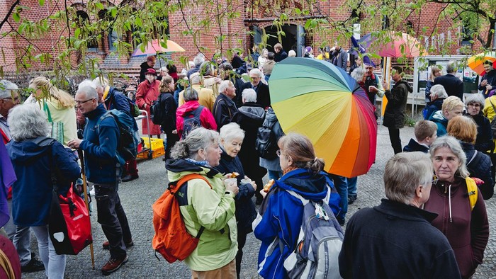 Eine Gruppe von Menschen steht beisammen, einige halten Regenschirme, darunter ein bunter Regenschirm.