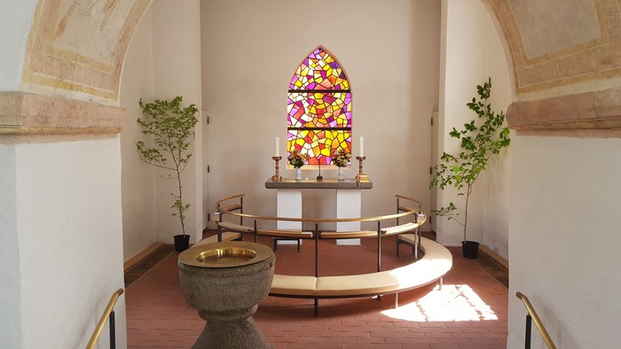 Kapel med farverige vinduesglas, alter, bænke og to planter