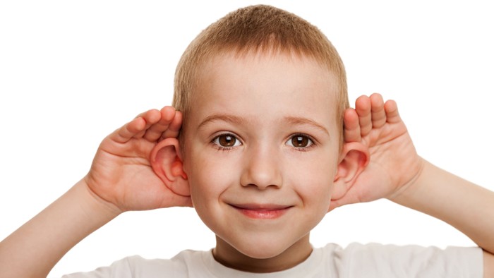 Et lille barn med hænderne ved ørene, smilende.