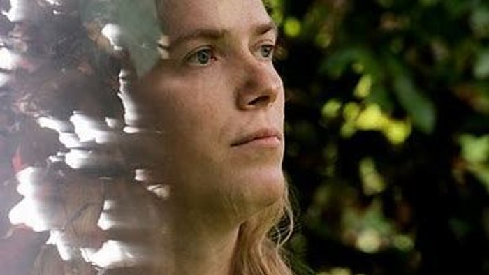 En kvinde med blond hår ser træt ud og ser ud af et vindue med blomster.