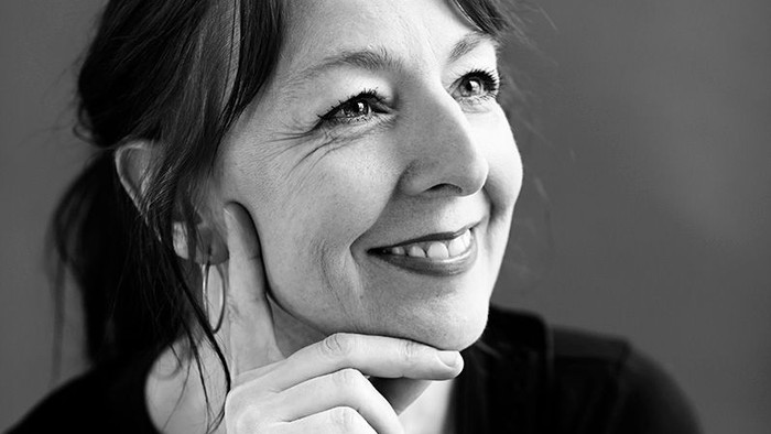 En kvinde med kort hår, der smiler og har hovedet på hånd.