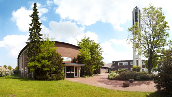 Das Bild zeigt ein Gebäude mit einer Kuppel und einem Turm, umgeben von Grünflächen und Bäumen.