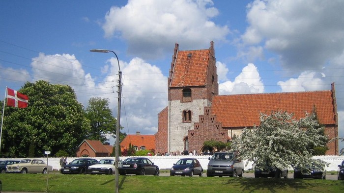 En kirke med røde tag og flere biler parkeret foran