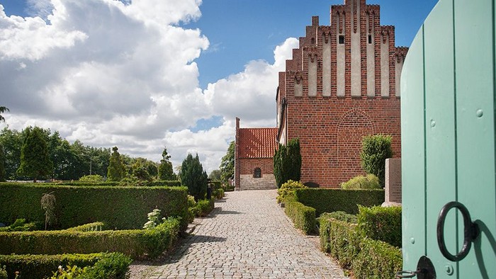 En smuk slot med mursten og tegl, omgivet af en grøn have og en sti.