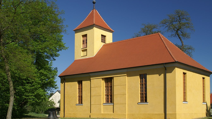 Kleine gelbe Kirche mit rotem Dach und Turm unter blauem Himmel