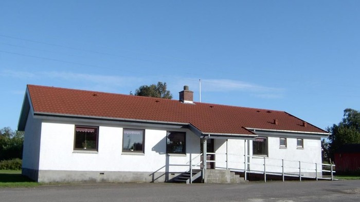 En hvid hytte med rødt tag og en trappe til indgangen.