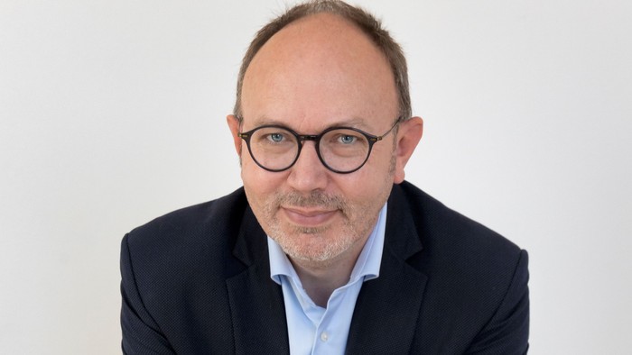 Mand i mørk jakke og briller sidder med hænderne på knæene.