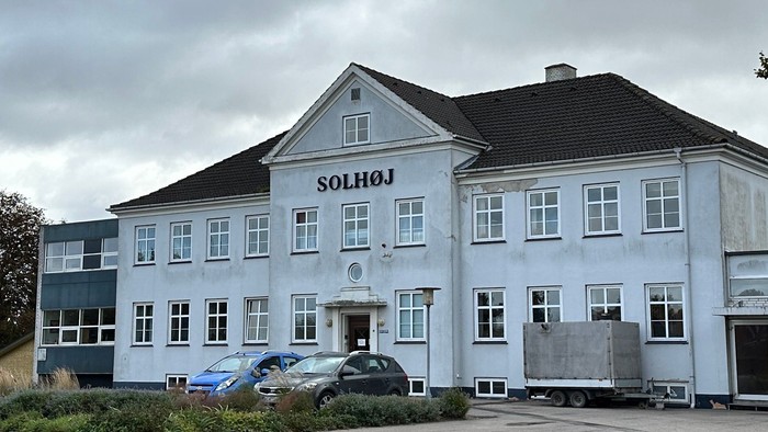 Et stort, blåmalet hus med navnet 'Solhøj' på facaden, med en dansk flag på en stang foran.