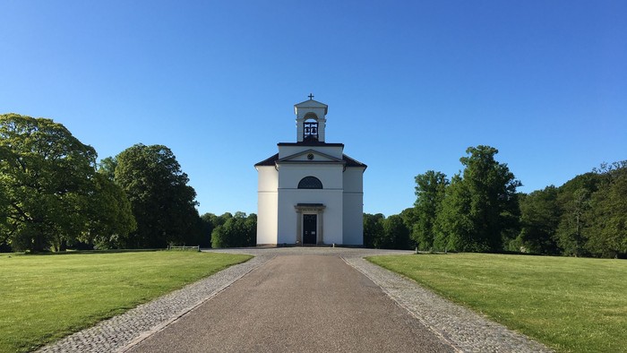 En lille, hvid kirke med tårn i en grøn park med træer.