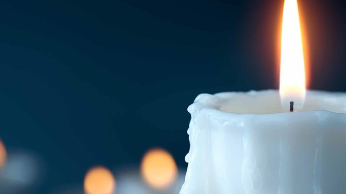 A lit candle with dripping wax, surrounded by other candles in a dark background.