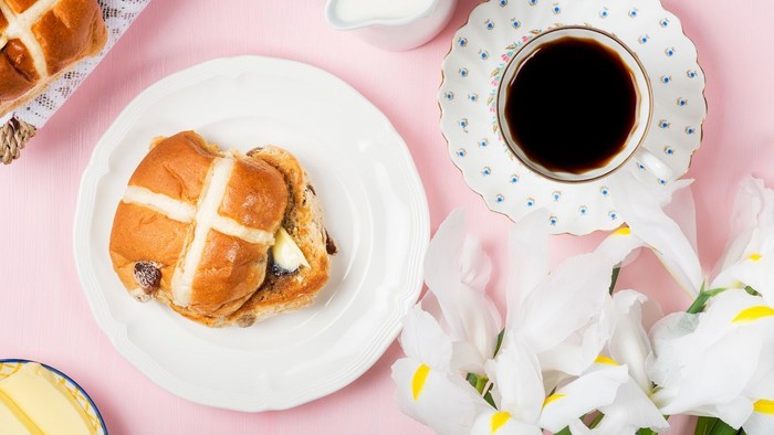 Ein Frühstückssetting mit Hefezopf, Kaffee und Blumen auf rosa Tischdecke