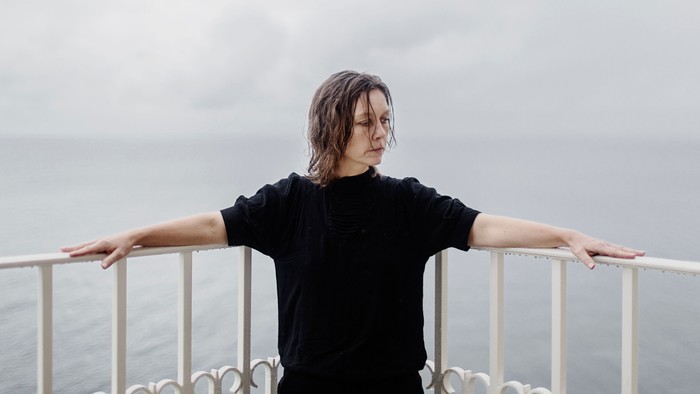 En ung person med langt mørkt hår står ved en balustrade og kigger ud over havet.