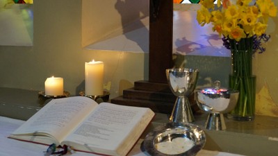 Ein Altar mit brennenden Kerzen, einem Buch, Kelchen und einer Vase mit gelben Blumen