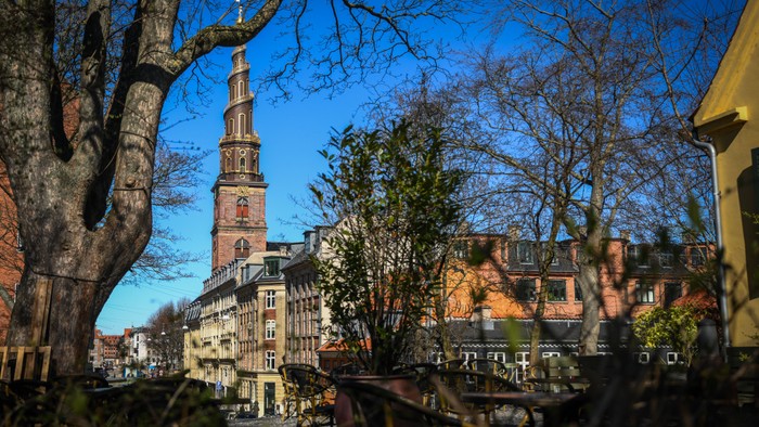 En kirke med høj tårn og murstensgårde under et blåt himmel.