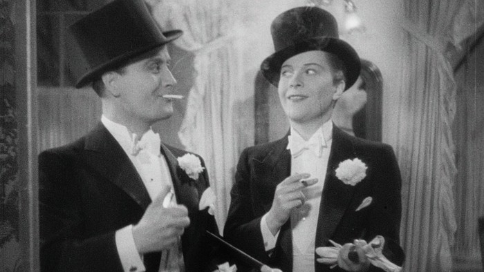 Zwei Männer im Frack und Zylinder posieren mit Blumen.