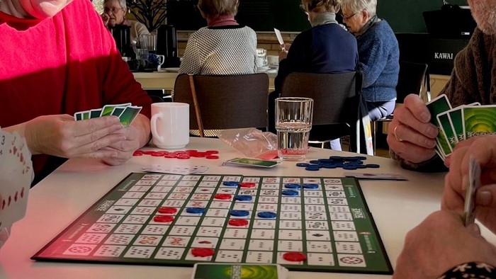 En gruppe ældre spiller Scrabble og kortspil på en bord.
