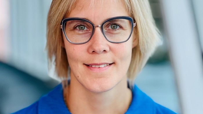 En kvinde med kort hår og briller, der smiler og ser direkte i kameraet.