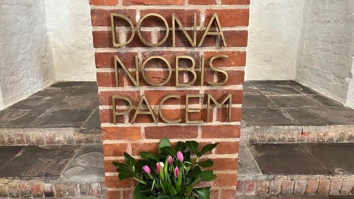 Ein Blumenstrauß vor einer Ziegelmauer mit lateinischem Text