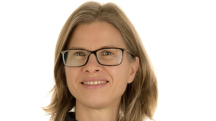 En kvinde med kort, blond hår og briller smiler til kameraet.